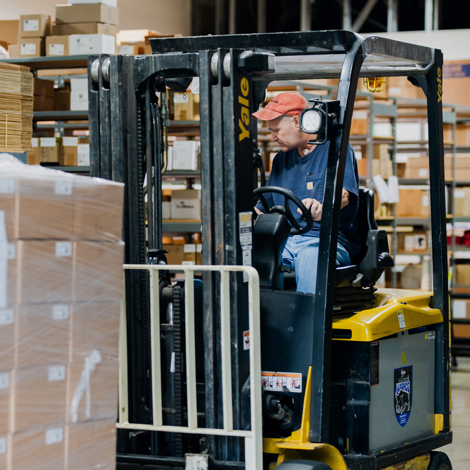 Employee driving forklift moving customers product for shipment Employee driving forklift moving customers product for shipment